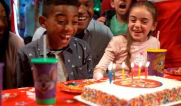 3 Kids smiling and sitting in front of a birthday cake