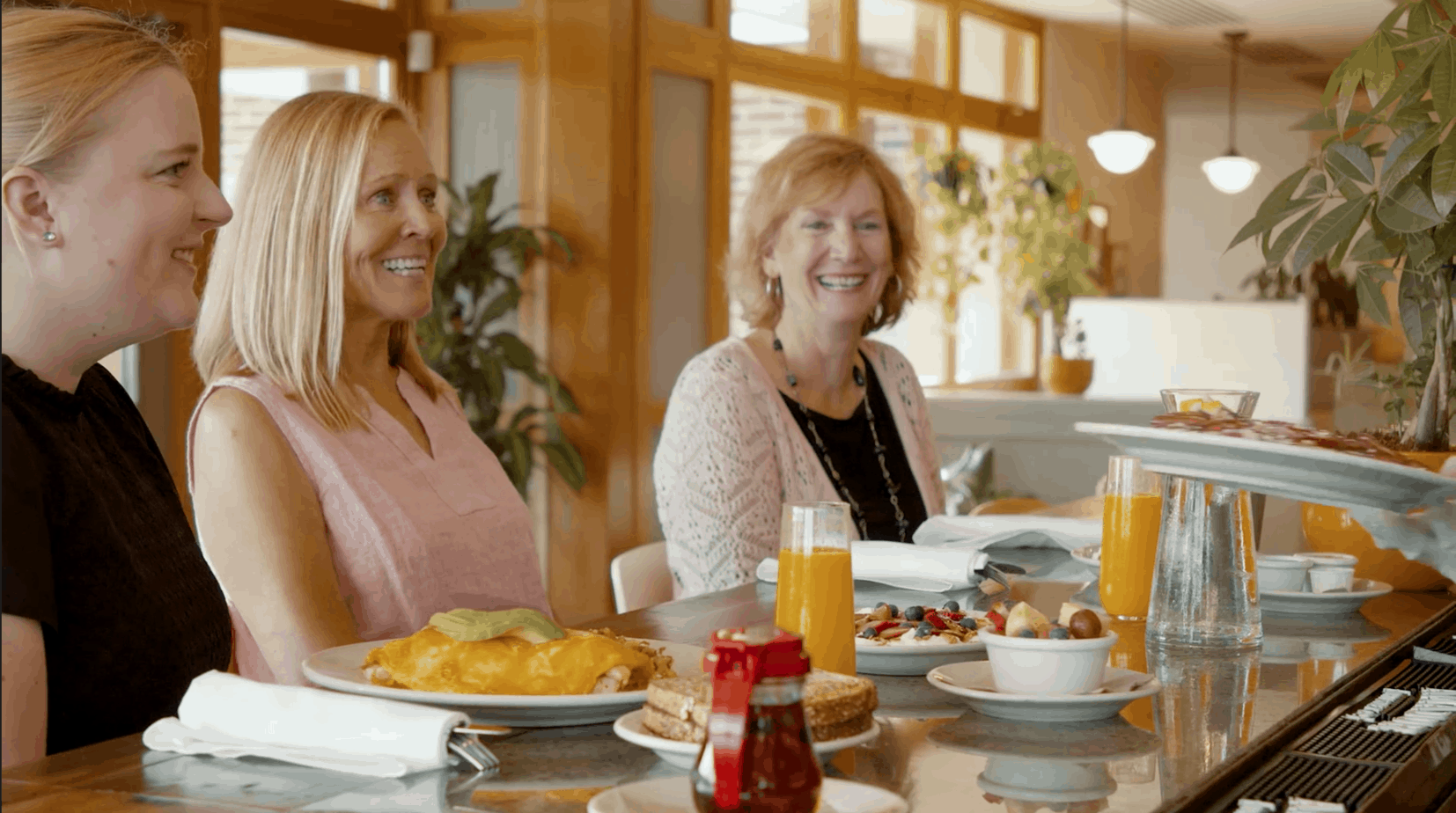 3 Women smiling at something off-camera with plates of food in front of them